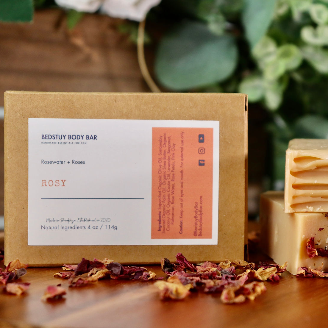 Stack of soap bars with a box labeled 'ROSY' on a wooden surface with greenery in the background.