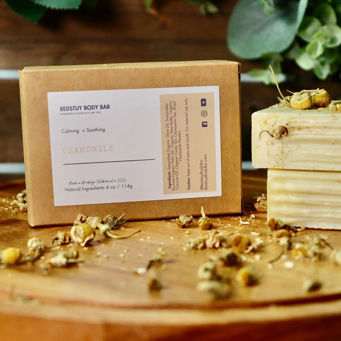 Two soap bars on a wooden surface with a label and dried flowers.